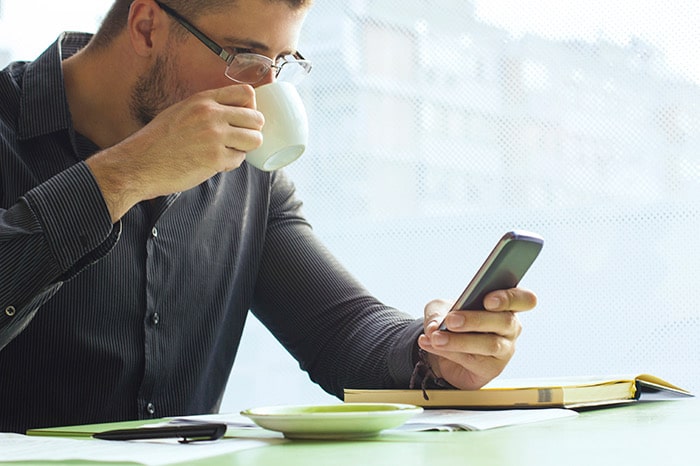 man drinking coffee while looking at cell phone